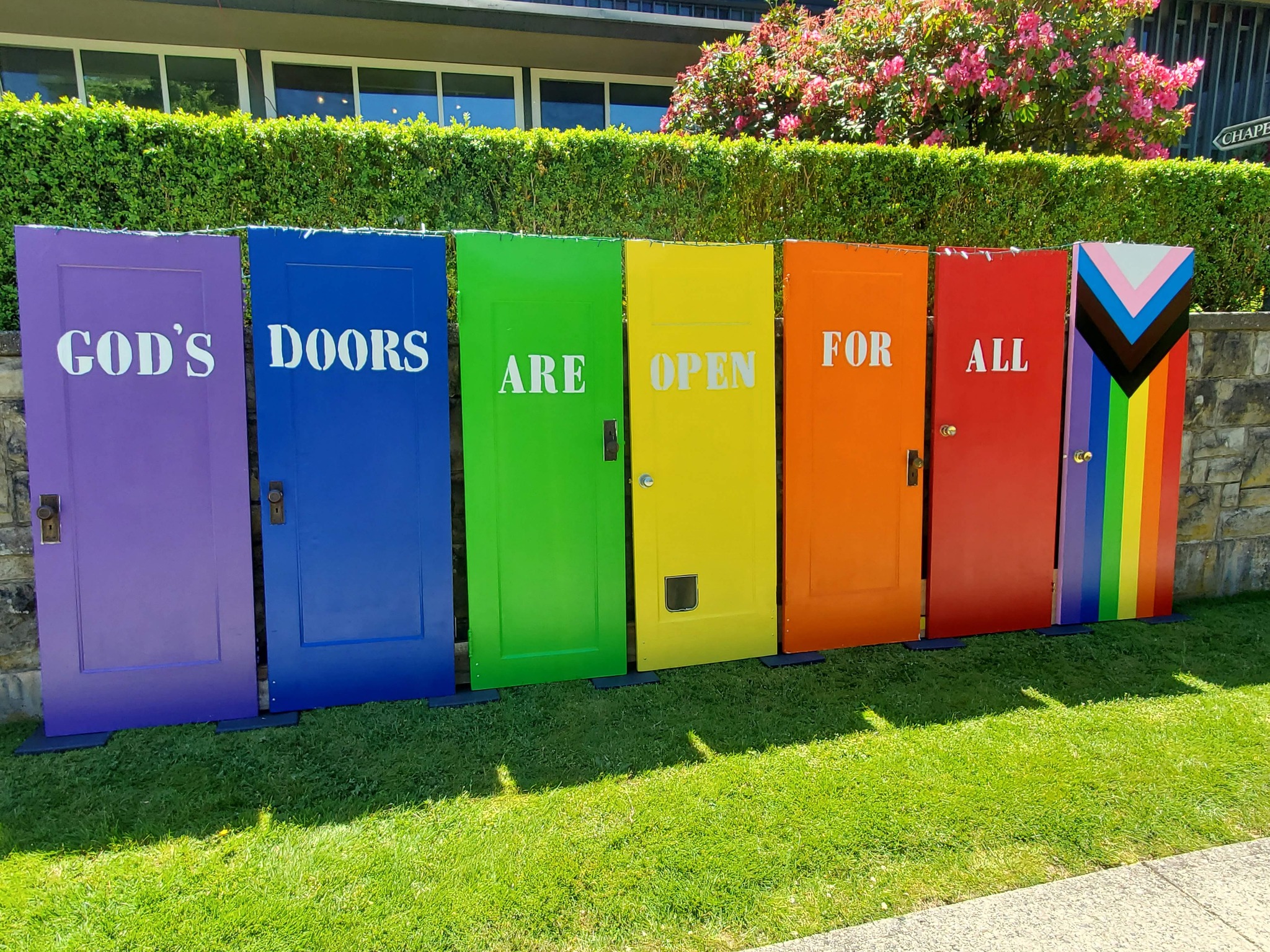 Doors painted in rainbow colours are lined up and on them is written "God's doors are open for all".