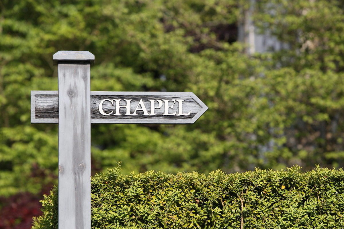 A wooden sign in front of greenery points the way to the Chapel.